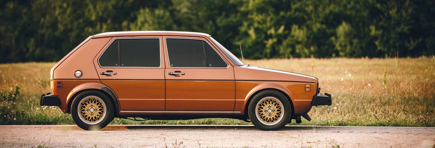Bronze first-generation Volkswagen Rabbit parked on a road beside a grass field
