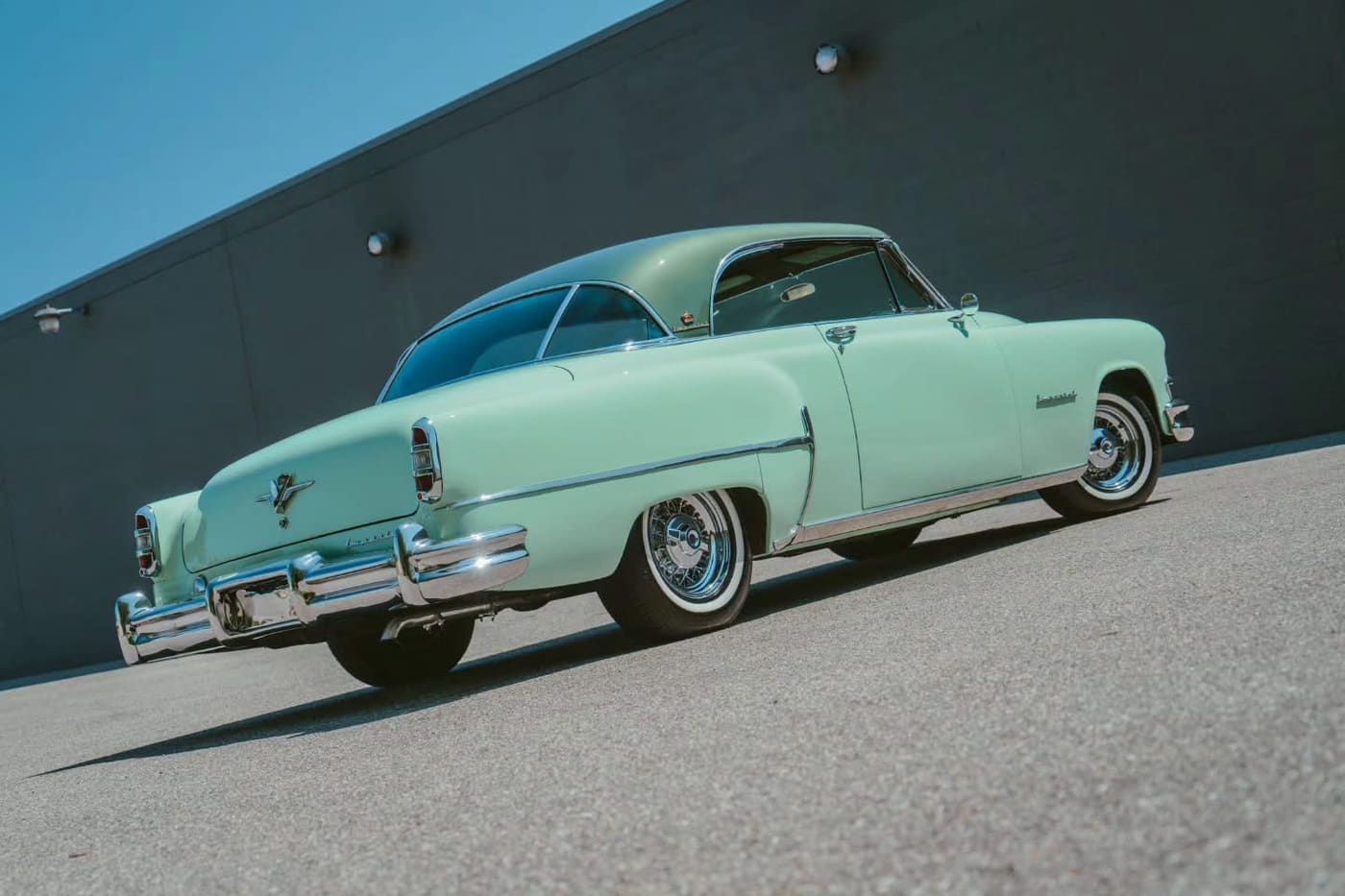 Pastel green 1950s two-door hardtop parked beside a gray building
