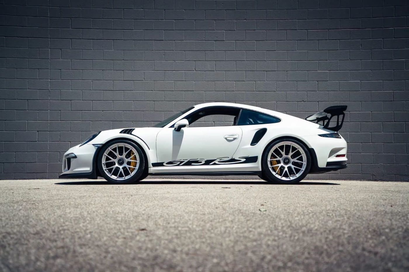 White Porsche 911 GT3 RS in profile against a gray brick wall