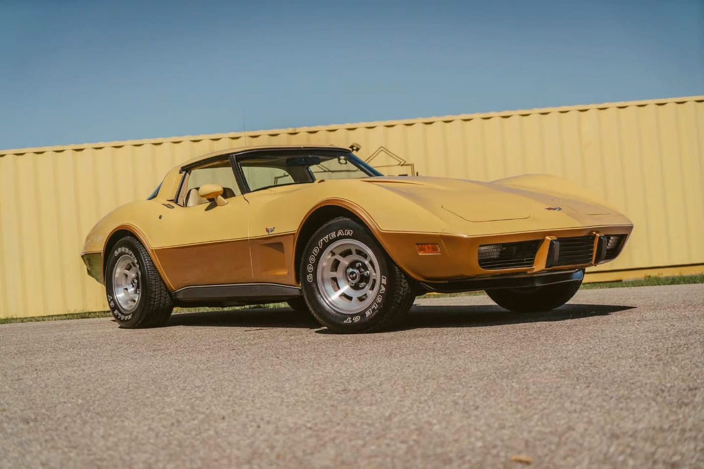 Gold Chevrolet Corvette parked in front of a yellow corrugated-metal building