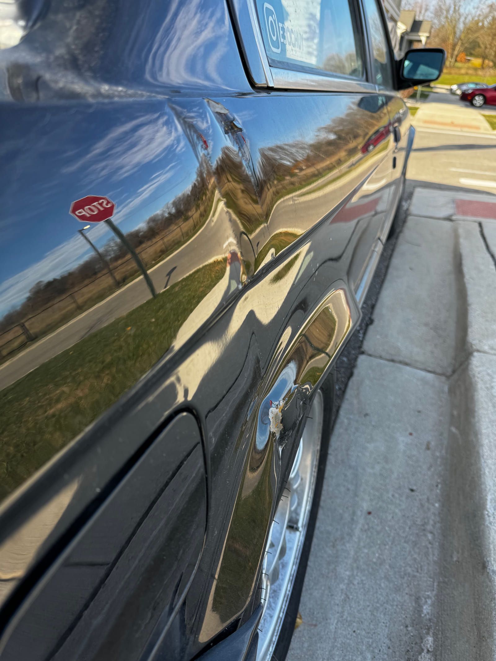 Close view along the side of the black BMW 325i showing a dent above the rear wheel arch