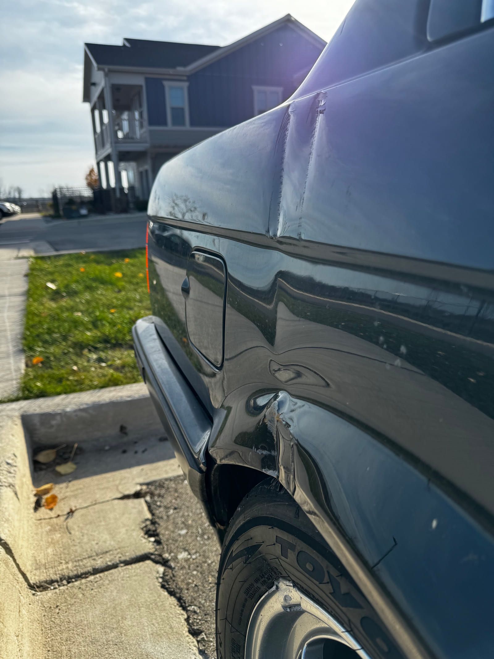 Rear quarter panel of the black BMW 325i showing a crease and damage above the wheel arch