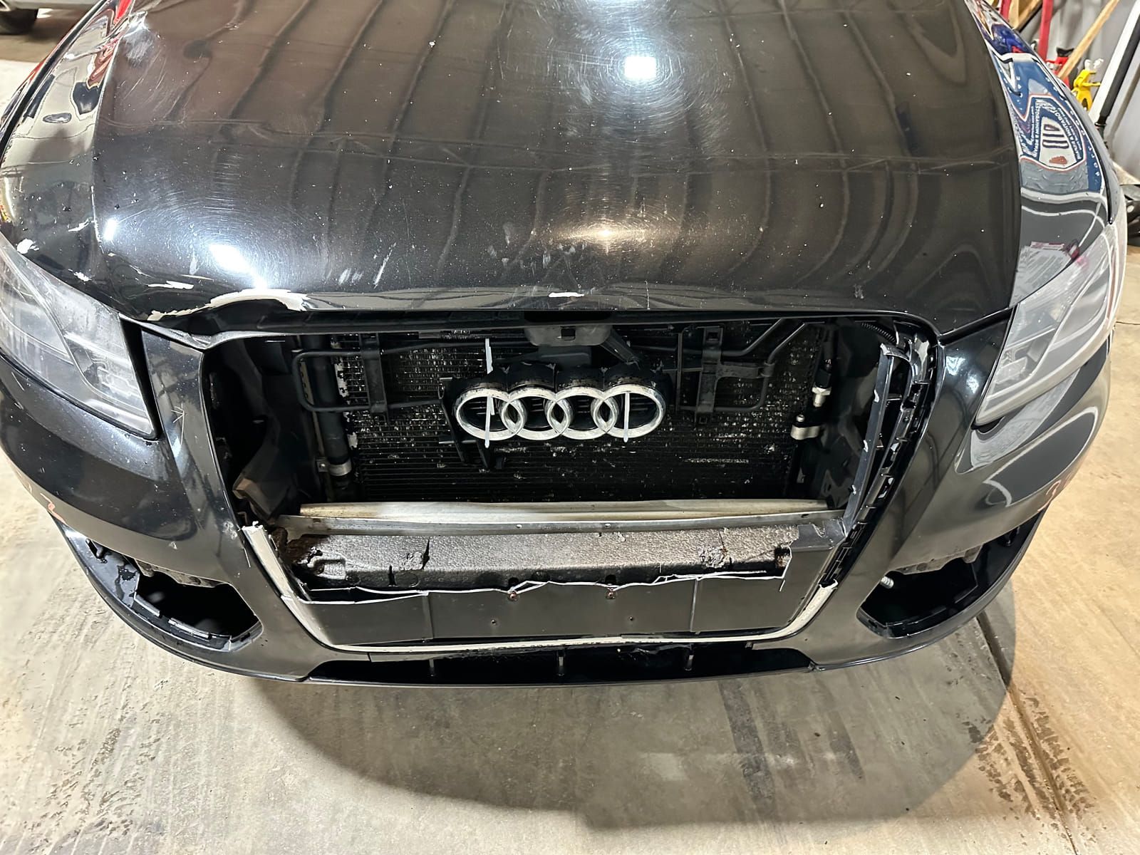 Front of a dark 2013 Audi Q5 with the bumper cover removed, showing damage to the front structure and cooling stack