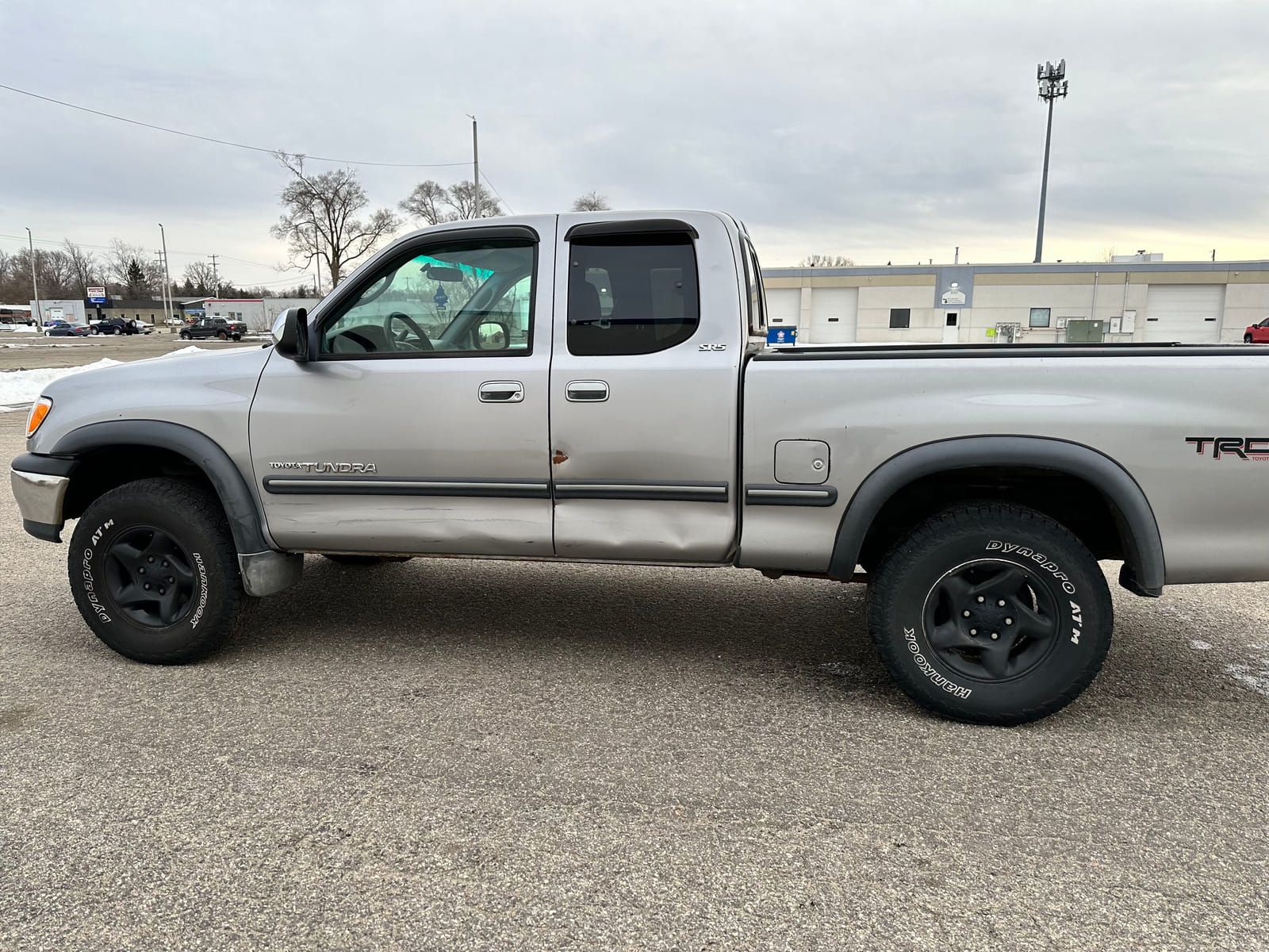 Silver 2003 Toyota Tundra extended cab, driver's side, showing damage along the lower door and rocker