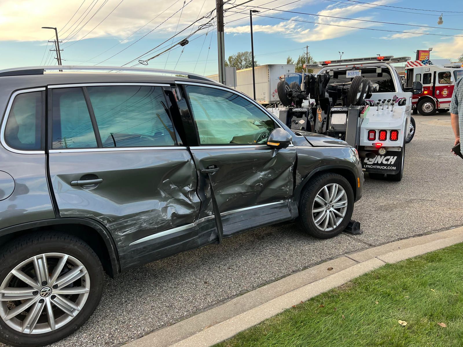 Gray 2015 Volkswagen Tiguan on a flatbed tow truck, showing a crushed driver-side rear door and quarter panel