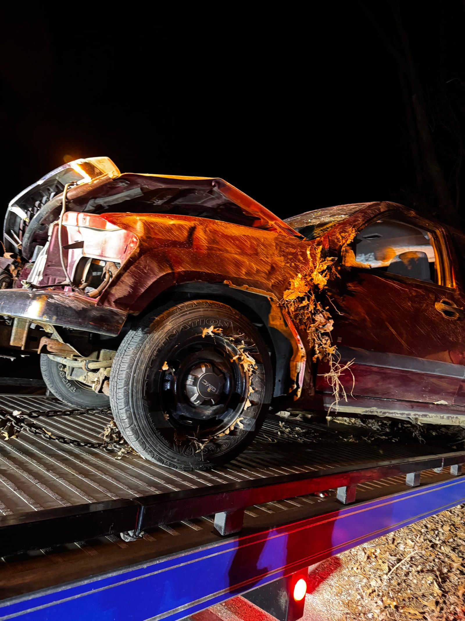 Wrecked 2006 Chevy Colorado on a flatbed tow truck at night, the passenger side crushed and caved in from a rollover